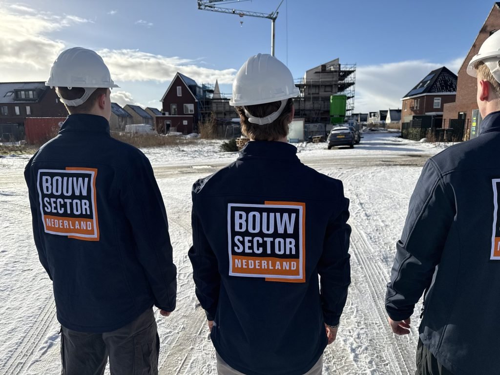 Drie vakmensen van Bouwsector Nederland met witte helm en logo op de jas in een nieuwbouwwijk in de sneeuw